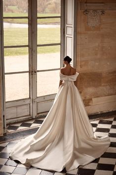 a woman in a wedding dress standing by an open door with her back to the camera