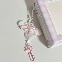 a pink keychain with a bow and heart on it sitting next to a box