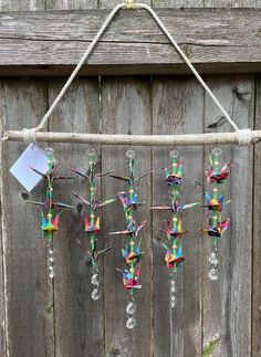 a wind chime hanging from a wooden fence with glass beads and paper cranes attached to it