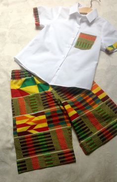 Shirt and shorts Kente boy's outfit.  This will make your child look very distinctive. The shirt is white, short sleeved with kente trim on pocket and cuff and with a kente panel in the back, and the shorts are in the matching kente fabric with an elasticated waist. Available from 3-5 years old. White Short Sleeve Sets With Pockets, White Sets With Pockets And Short Sleeves, White Short Sleeve School Sets, Baby African Clothes, Ankara Styles For Kids, Black Kids Fashion, African Dresses For Kids, African Inspired Clothing, African Print Dress Designs