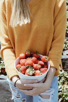 a woman holding a bowl full of strawberries