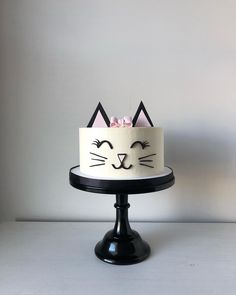 a white cake with black cat ears and pink flowers on top is sitting on a pedestal