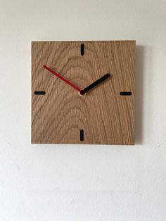 a square wooden clock with red hands and black numbers on the face against a white wall