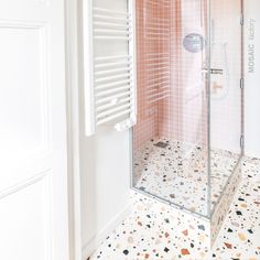 a walk in shower sitting next to a white wall and tiled floor with pink tiles on the walls