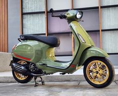 a green scooter parked in front of a building with yellow rims on it