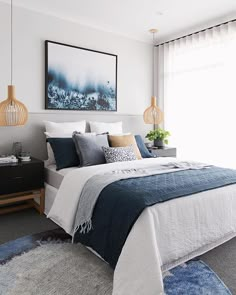 a bedroom with blue and white bedding, rugs and artwork on the wall