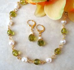 This classic beaded necklace features beautiful green Peridot gemstones and ivory freshwater pearls. Necklace is finished with a lobster closure. The necklace measures 18 inches in length. This simple yet elegant pair of earrings features green Peridot gemstone drop with a tiny freshwater pearl. Hanging from a surgical steel lever-back, it measures 1.25 " in length. Earrings are light weight and sway gracefully as you move about your day. This beautiful necklace is unique, feminine and eye-catching, Perfect for everyday or anyone to wear to a special occasion! Green Pearl Necklace With Round Beads And Pearl Drop, Green Pearl Drop Jewelry With Round Beads, Handmade Green Peridot Jewelry, Green Pearl Round Beads Jewelry, Elegant Peridot Round Beads Jewelry, Peridot Gemstone Beads Jewelry, Peridot Gemstone Beads Necklace For Gift, Green Peridot Gemstone Beads Jewelry, Pearl Jewelry Set