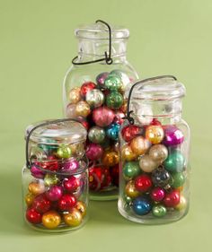 three glass jars filled with ornaments on top of a green surface