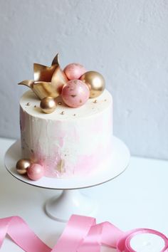 a white cake with pink and gold decorations on top, next to a pink ribbon