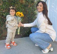 a woman kneeling down next to a little boy with flowers in his hand and smiling at the camera