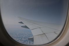 the wing of an airplane as seen from inside it's window, with clouds below