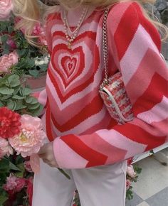 a blonde haired woman wearing a red and white striped sweater holding a pink heart shaped purse