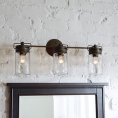 a bathroom vanity with three mason jars on the light fixture and a mirror above it