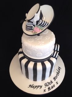 a three tiered cake with black and white stripes on the bottom, topped with a hat