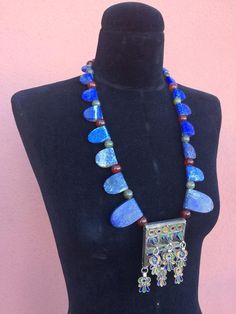 REDUCED from $650Striking necklace composed of  large one-side-rounded, one-side-straight, slabs of gorgeous raw matte Lapis Lazuli in graduated sizes (largest to the front), separated by green Labradorite & Carnelian ball-shaped-beads, framing a fabulous Moroccan Berber enamel & tribal-silver-metal prayer-amulet/talisman pendant box with 6 freely dangling parts, also in matching tribal-silver-metal & enamel, that may be  abstracted Hamsa symbols or flowers(?).  Smaller Labradorite b Artisan Necklace For Ceremonial Occasions, Unique Blue Necklace With Inlay, Artisan Lapis Lazuli Pendant Necklace, Handmade Lapis Lazuli Jewelry For Festivals, Traditional Handmade Necklace With Rectangular Pendant, Handmade Traditional Necklace With Rectangular Pendant, Unique Blue Ceremonial Jewelry, Blue Spiritual Necklaces For Rituals, Unique Blue Jewelry For Ceremonial Occasion