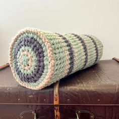 a crocheted blanket sitting on top of an old brown piece of leather luggage