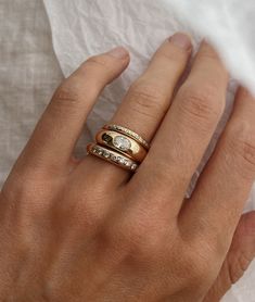 a woman's hand with two gold rings on top of each other and one diamond ring in the middle