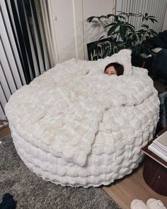 a woman is laying in a bed made out of fluffy white blankets on the floor