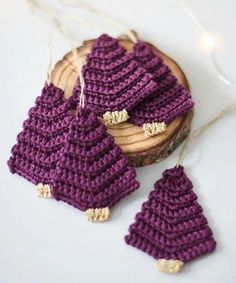 two crocheted christmas tree ornaments hanging from strings on a piece of wood with string