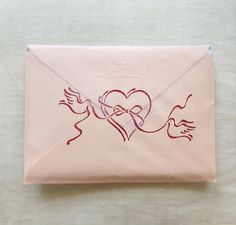 a pink envelope with a drawing of a heart and two hands holding a red ribbon