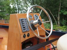 the steering wheel and dashboard of a wooden boat on water with trees in the background