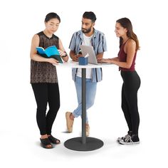 three people are standing around a table with a laptop and book on it, while one person is looking at the screen