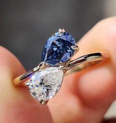 a person holding a blue and white ring with two pear shaped diamonds on it's sides