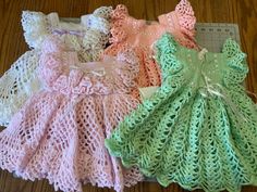 three knitted baby dresses sitting on top of a wooden table