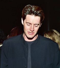 a man in a black shirt and tie looking at his cell phone while standing next to other people