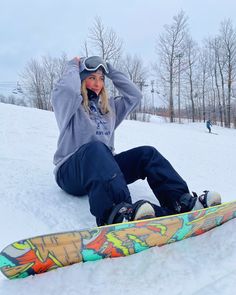 a woman sitting in the snow next to a snowboard