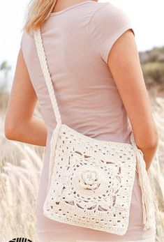 a woman carrying a white crocheted bag in the middle of a wheat field