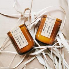 two candles sitting next to each other on top of a white cloth covered bed sheet