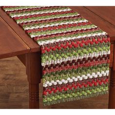 a table runner with red, green and white designs on it sitting on top of a wooden table