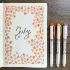 an open notebook with three markers next to it and the word july written in cursive writing