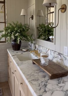 a bathroom with marble counter tops and two mirrors on the wall above it, along with vases filled with flowers