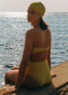 a woman in a yellow bathing suit sitting by the water