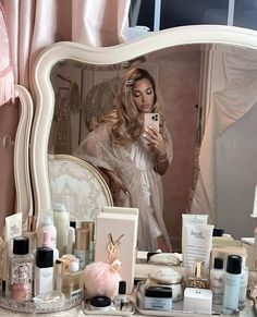 a woman taking a selfie in front of a mirror with cosmetics and makeup products on it