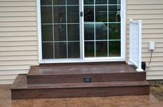 a wooden deck with steps leading up to the front door and side window on top of it