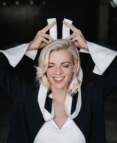 a woman with blonde hair wearing a black suit and white shirt holding her hands above her head