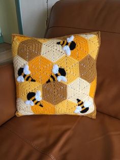 a crocheted honeycomb pillow on a brown leather couch with white and black bees