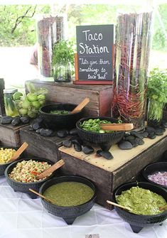 an assortment of food is displayed on a table in front of a sign that says taco station