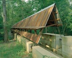 a wooden structure sitting in the middle of a forest next to a cement wall and trees