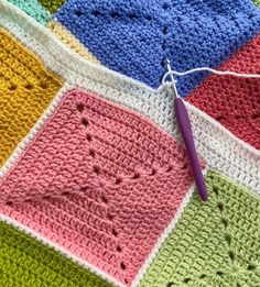 a crocheted blanket with a purple needle on top of it and several squares of different colors