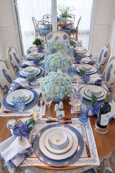 a dining room table set with blue and white plates, silverware, and flowers