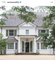 a large white house with lots of windows and shutters on the front door is surrounded by trees