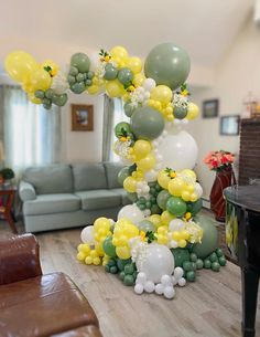 the balloon arch is decorated with yellow and green balloons, greenery, and flowers