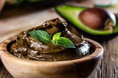 a wooden bowl filled with chocolate pudding next to an avocado