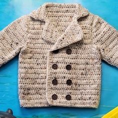 a crocheted sweater with buttons on the front and back, sitting next to a toy car