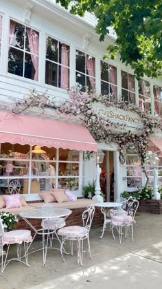 an outdoor cafe with tables and chairs in front of the storefront, pink flowers on the awning