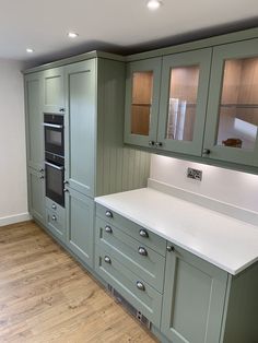 an empty kitchen with green cabinets and white counter tops, wood flooring and hardwood floors